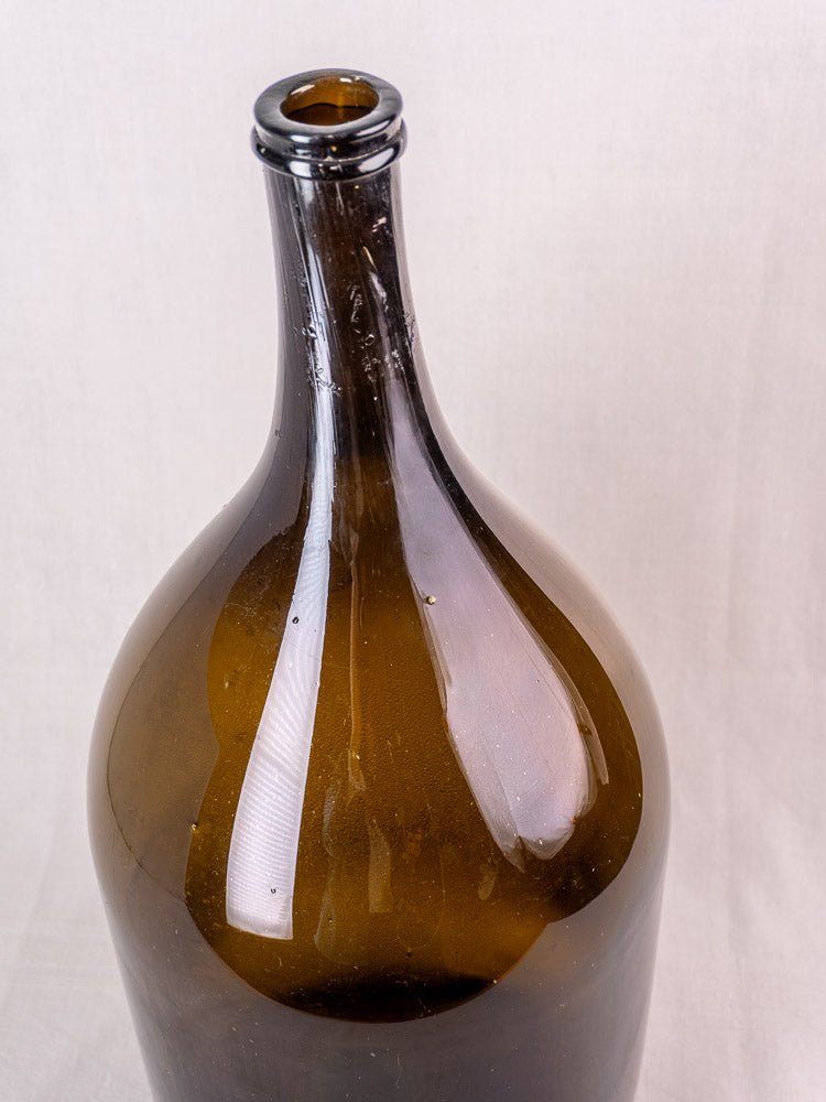 Antique French hand-blown olive green glass wine bottle with narrow neck, plain light background.