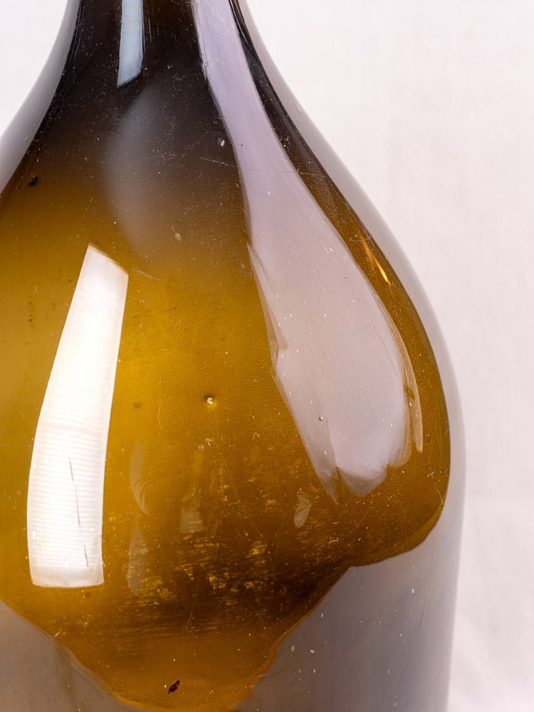 Antique French hand-blown olive green glass wine bottle with 19th-century reflections and subtle texture.