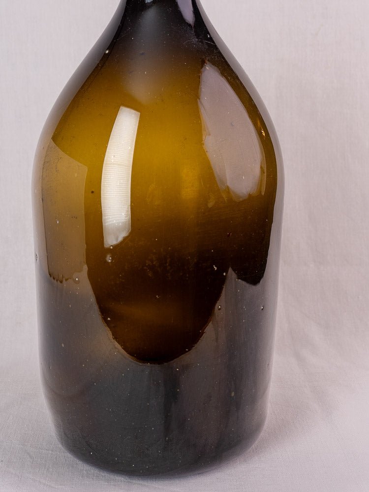 Antique French hand blown wine bottle with olive green glass and 19th-century detailing on white background.