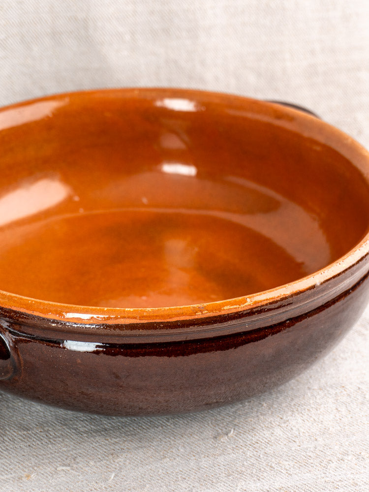 Mid 20th century antique French earthenware poêlon with brown glaze, caramel interior, on fabric surface.