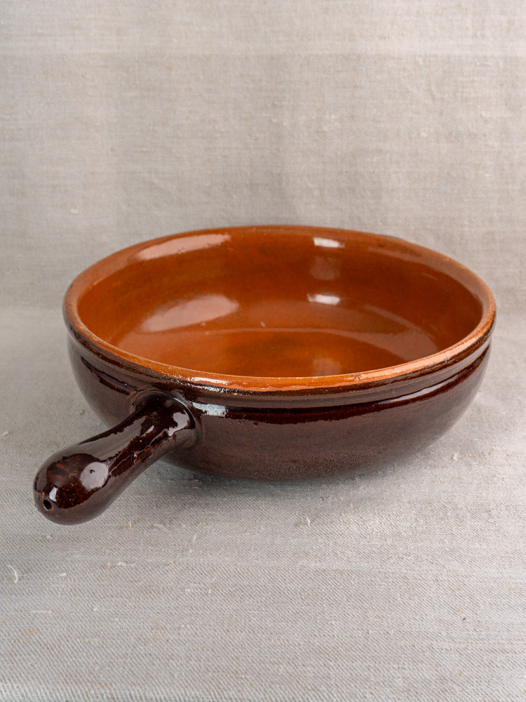Mid-20th century French earthenware poêlon with glossy brown glaze and caramel interior on light gray fabric.