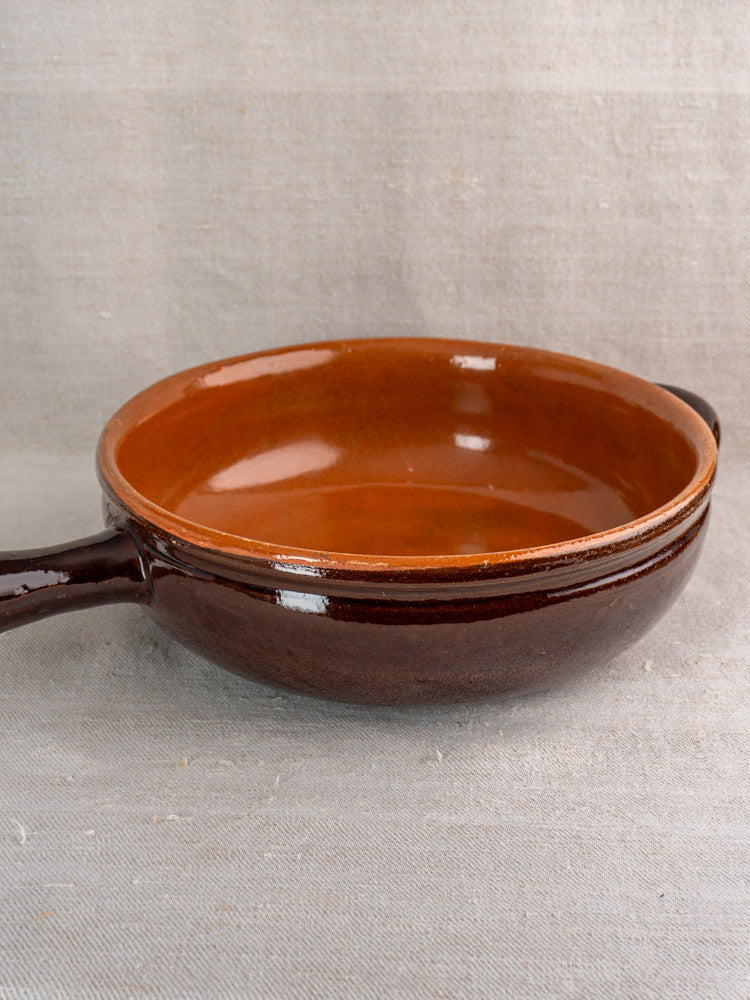 Antique French earthenware poêlon with handle, brown glaze and caramel interior, shown on light gray fabric.