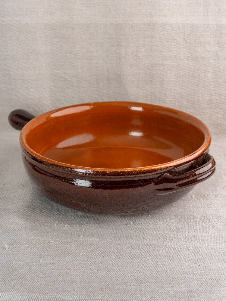Mid-century French earthenware poêlon, brown glazed with caramel interior and handles, on textured gray fabric.