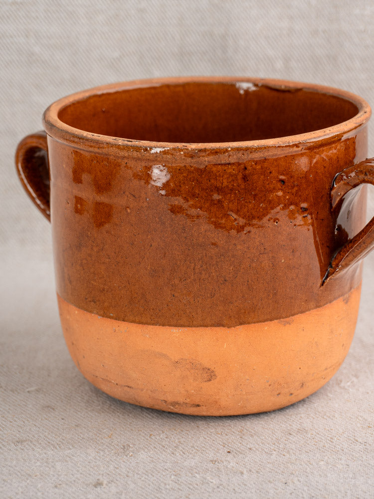 Antique French Digoin confit pot, brown glazed earthenware, side handles, unglazed bottom; displayed on textured fabric.