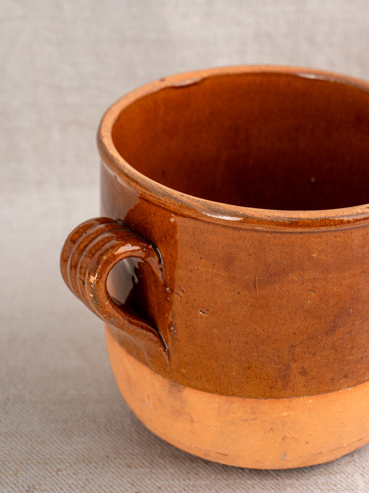 Antique French Digoin confit pot in glazed earthenware, rustic brown with glossy top, on neutral fabric background.