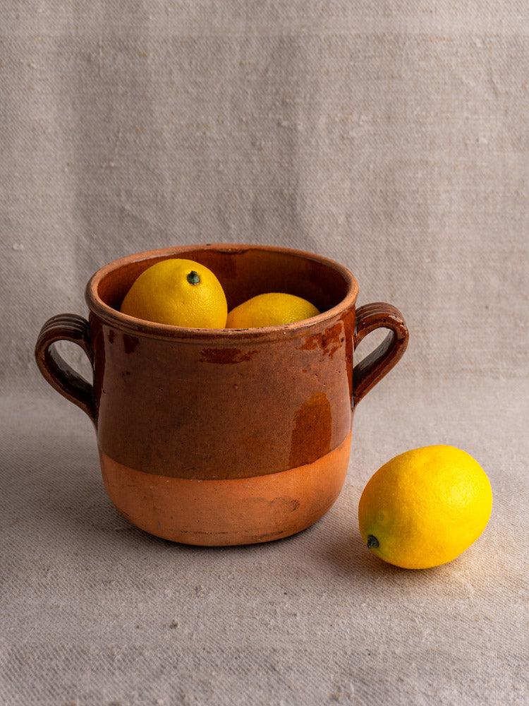 Antique French Digoin glazed earthenware confit pot with two handles, holding lemons on textured beige fabric.