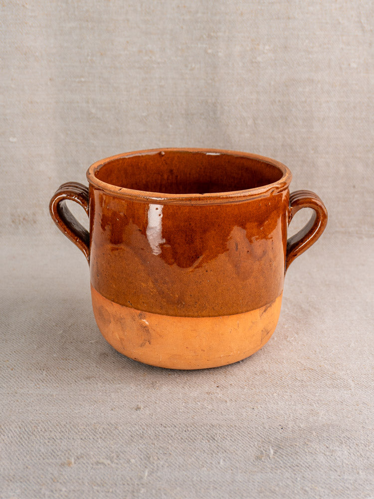 Mid 20th-century French glazed earthenware confit pot with two handles, glossy top, on neutral fabric background.