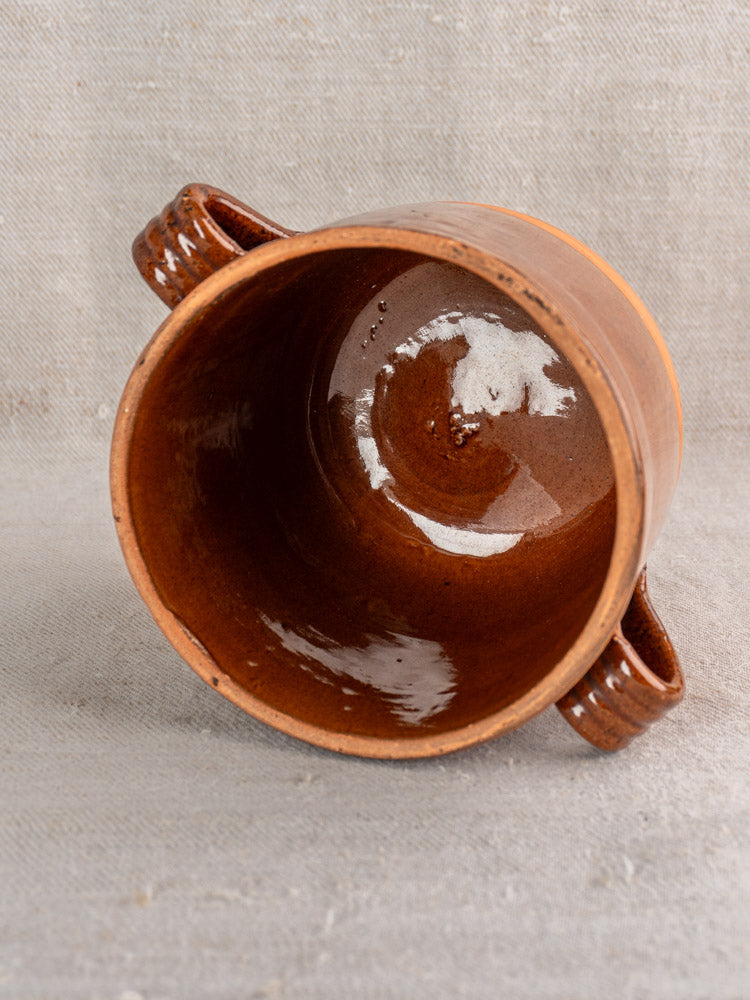 Mid-century French Digoin confit pot in glazed earthenware with brown interior, side handles, on light textured fabric.
