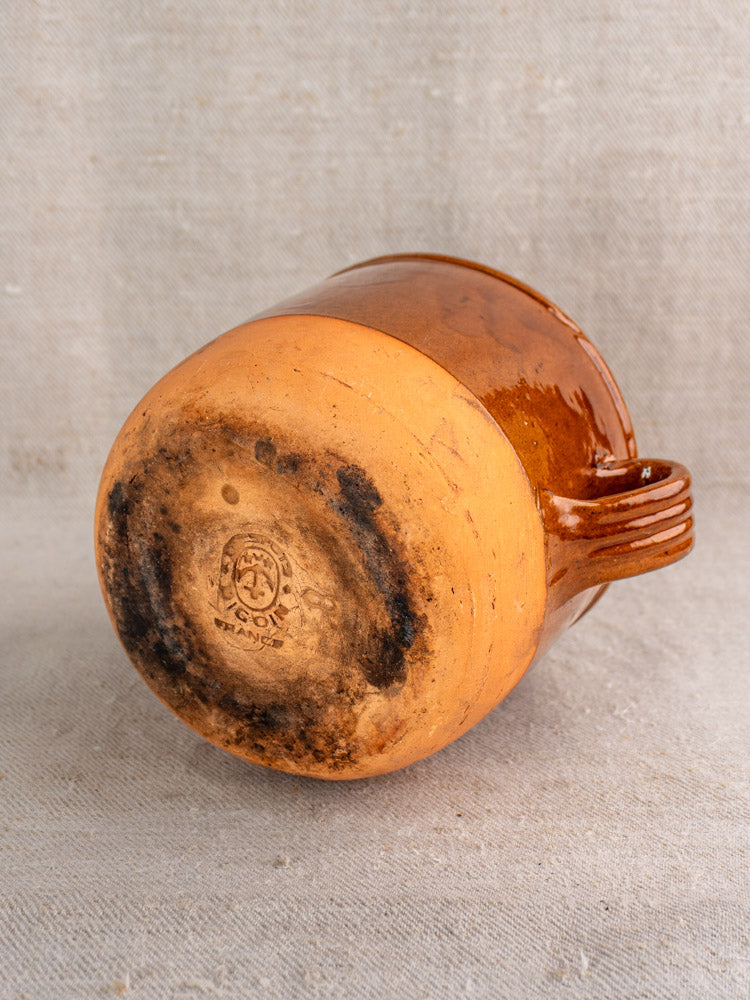 Mid-century French Digoin confit pot, brown glazed earthenware, side handle, unglazed base with black scorch marks on beige fabric.