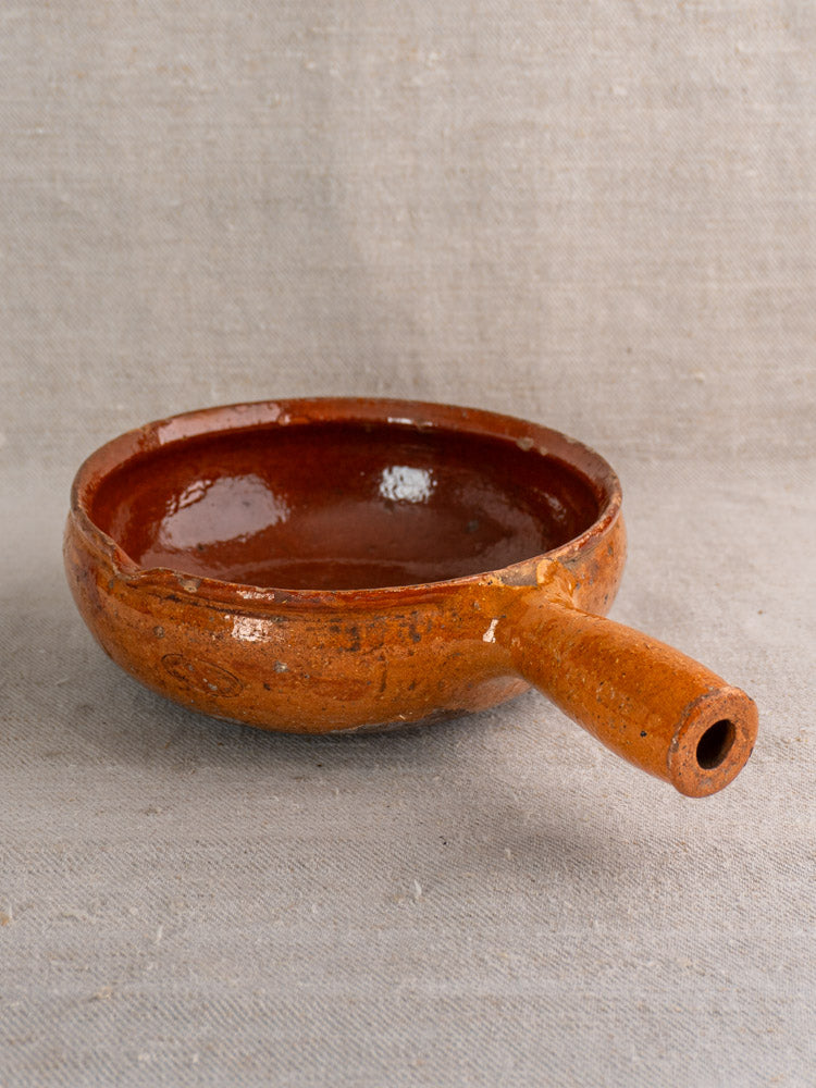 Antique French Vallauris glazed earthenware poêlon with short handle, displayed on textured gray fabric.