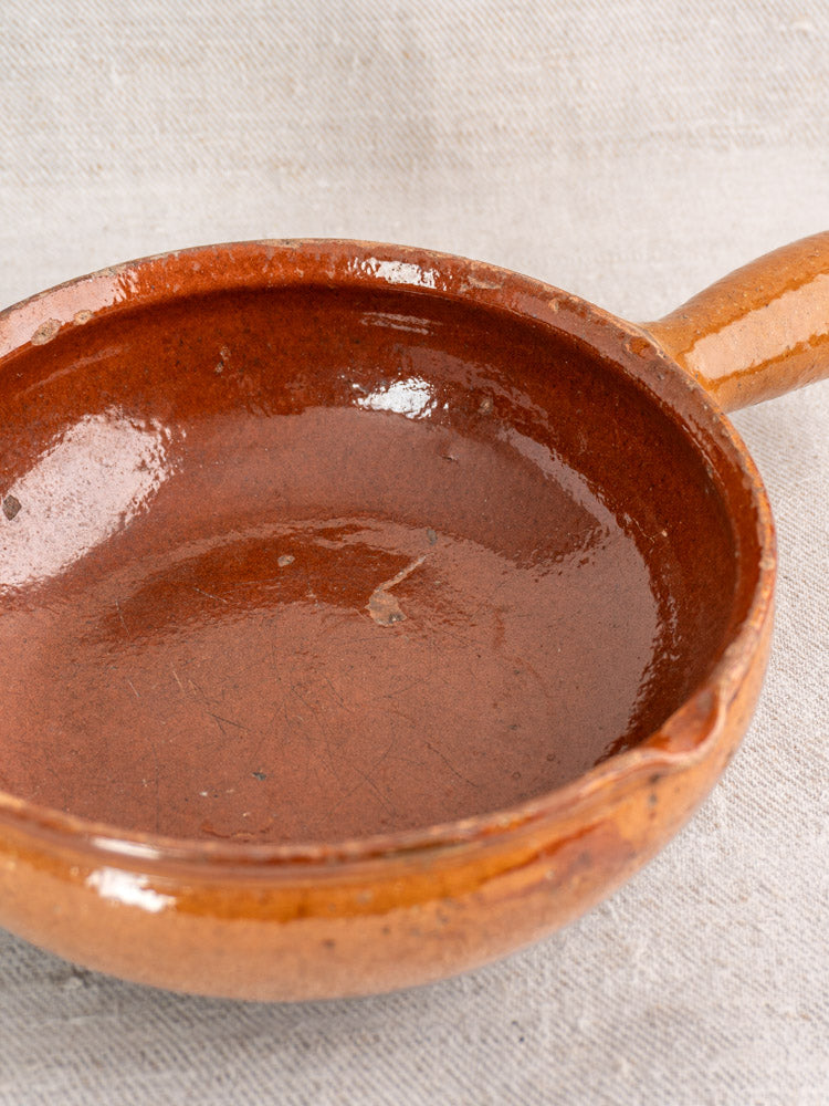 Antique French Vallauris glazed earthenware poêlon on light textured fabric; classic Provençal kitchenware.