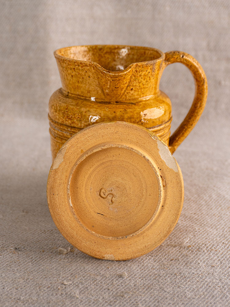 Antique French Pot à Lait with speckled yellow glaze, worn base, and stamped mark on textured surface.