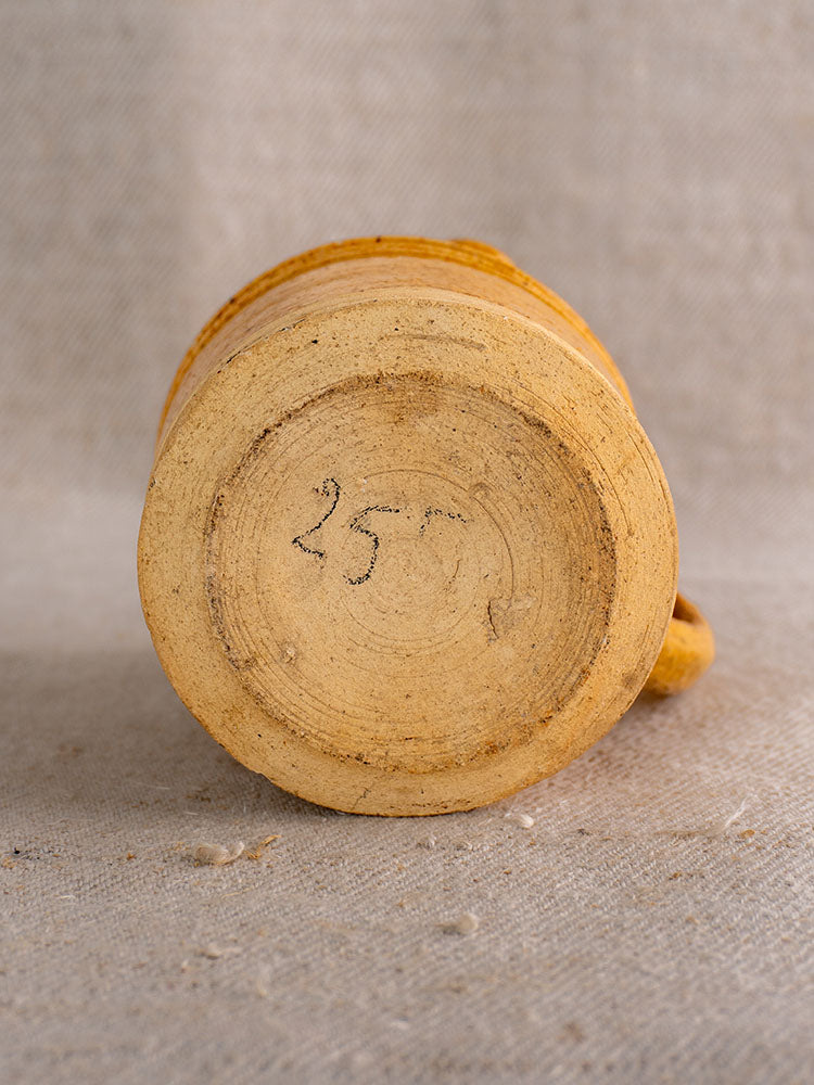 Antique French Pot à Lait base with speckled yellow glaze and black 257 mark on textured light fabric.