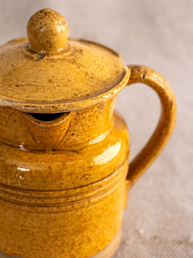 Antique French Pot à Lait with lid and handle, speckled yellow glaze, shown on a neutral textured background.