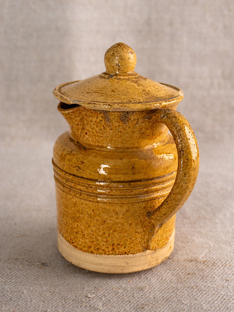 Antique French Pot à Lait with speckled yellow glaze, matching lid, and handle on light textured fabric.