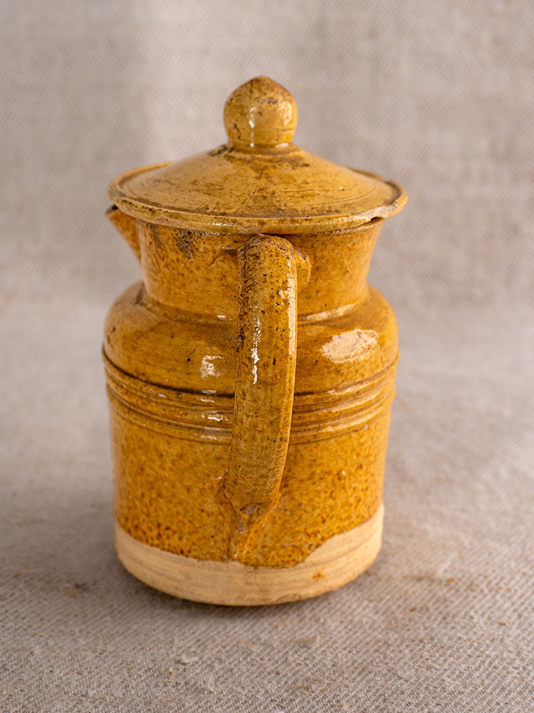 Antique French Pot à Lait with lid, curved handle, and speckled yellow glaze on textured beige fabric.
