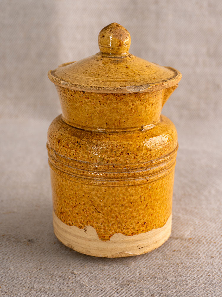 Antique French Pot à Lait with lidded, speckled yellow glaze and rustic grooves on beige textured fabric.