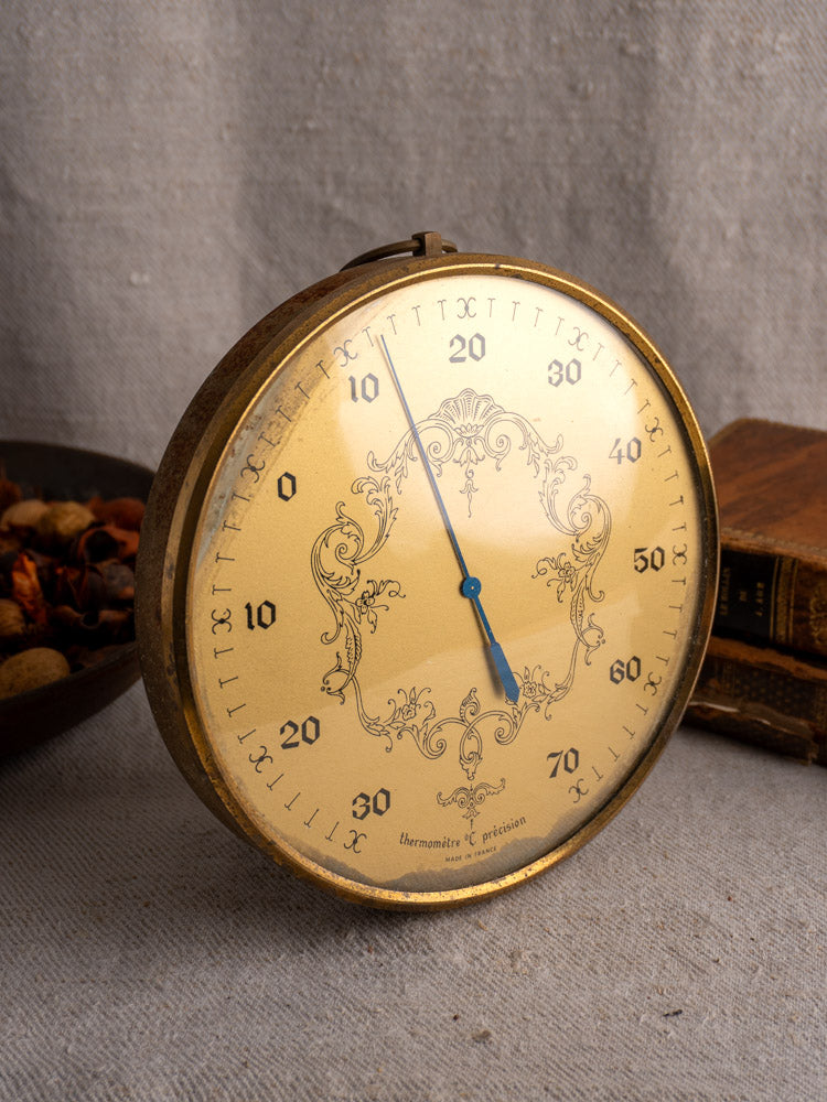 Vintage French Lincoln gilt wall thermometer with ornate gold details, shown with potpourri and antique books.