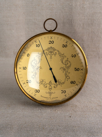 Vintage French gilt wall thermometer with ornate gold dial, Celsius display, on beige fabric background.