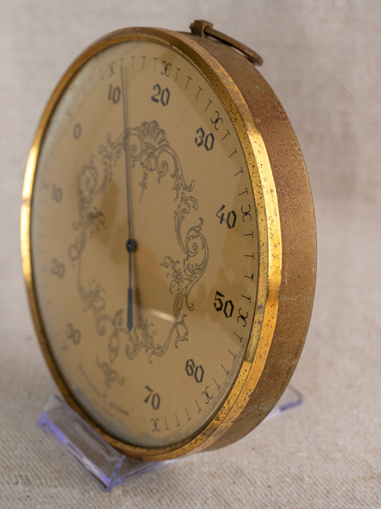 Vintage French gilt wall thermometer with ornate gold-toned details, displayed on a clear stand.