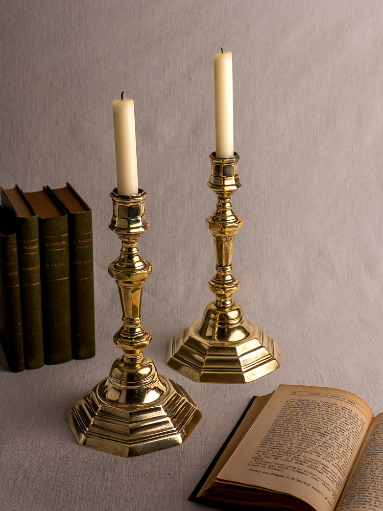 Pair of antique French brass candlesticks, Régence Period, hexagonal bases and ornate stems on gray surface.