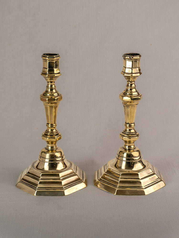 Pair of antique French brass candlesticks, Régence Period, hexagonal bases and ornate stems on gray surface.