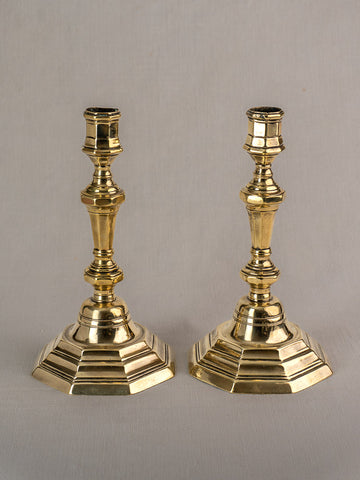Pair of antique French brass candlesticks, Régence Period, hexagonal bases and ornate stems on gray surface.