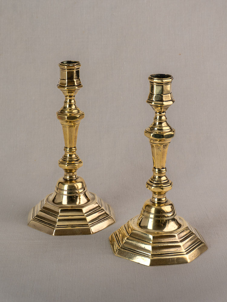 Pair of antique French Régence brass candlesticks with faceted stems and hexagonal bases on light gray background.