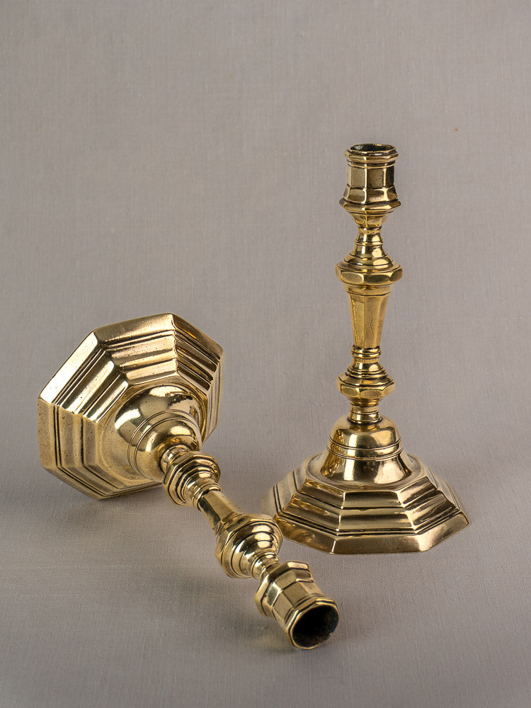 Antique French brass candlesticks, Régence period, ornate hexagonal bases; one upright, one lying on gray background.
