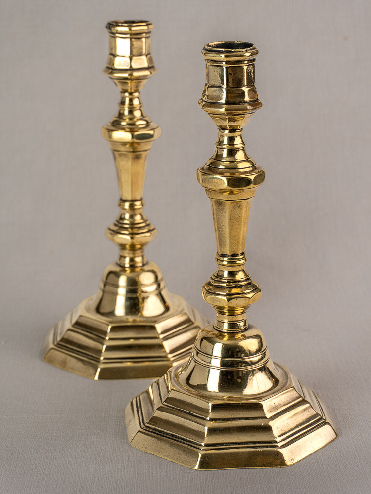Antique French brass candlesticks pair, Régence period, ornate hexagonal bases and faceted stems on gray surface.