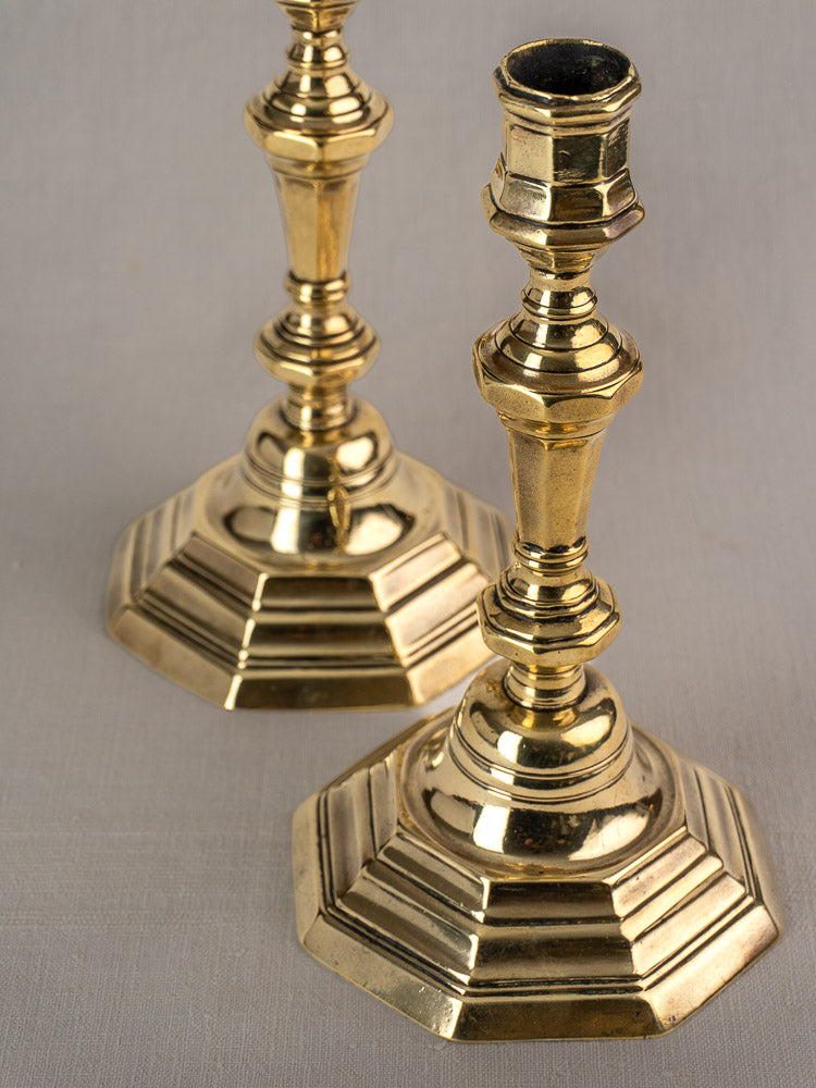 Pair of antique French Régence brass candlesticks with octagonal tiered bases on light gray surface.
