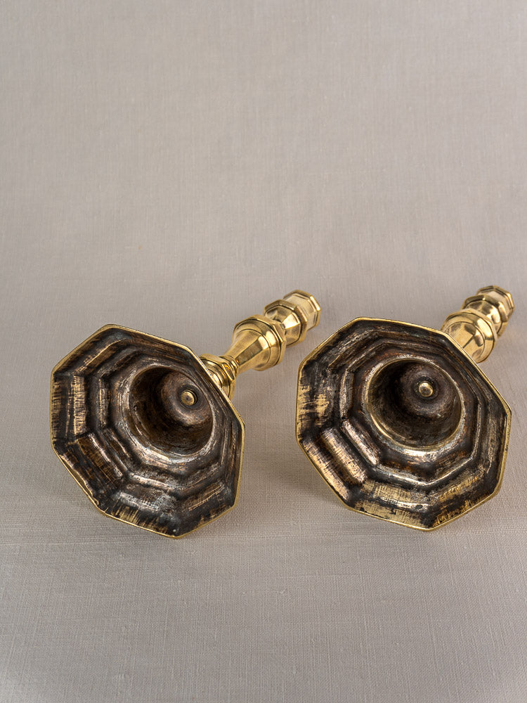 Pair of antique French brass candlesticks from the Régence period with hexagonal, tiered bases and aged patina on neutral fabric.