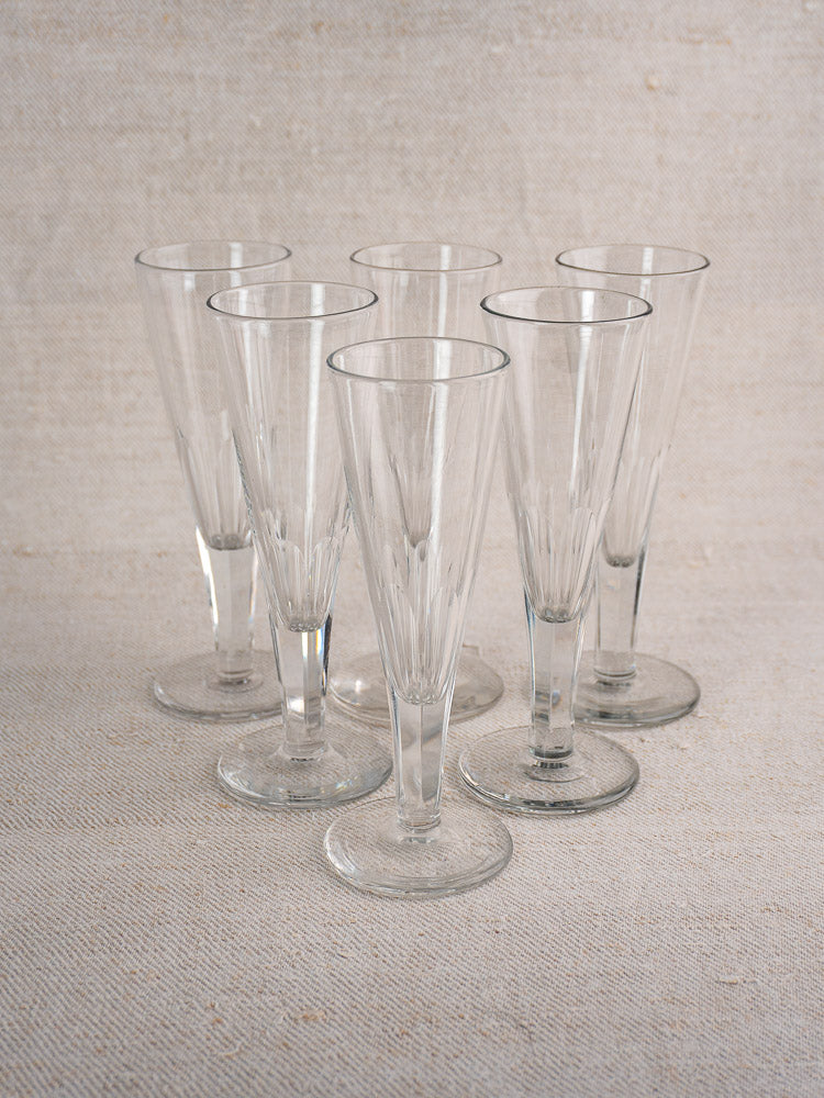 Set of six early 19th century antique French cut crystal champagne flutes on light beige textured surface with fabric backdrop.