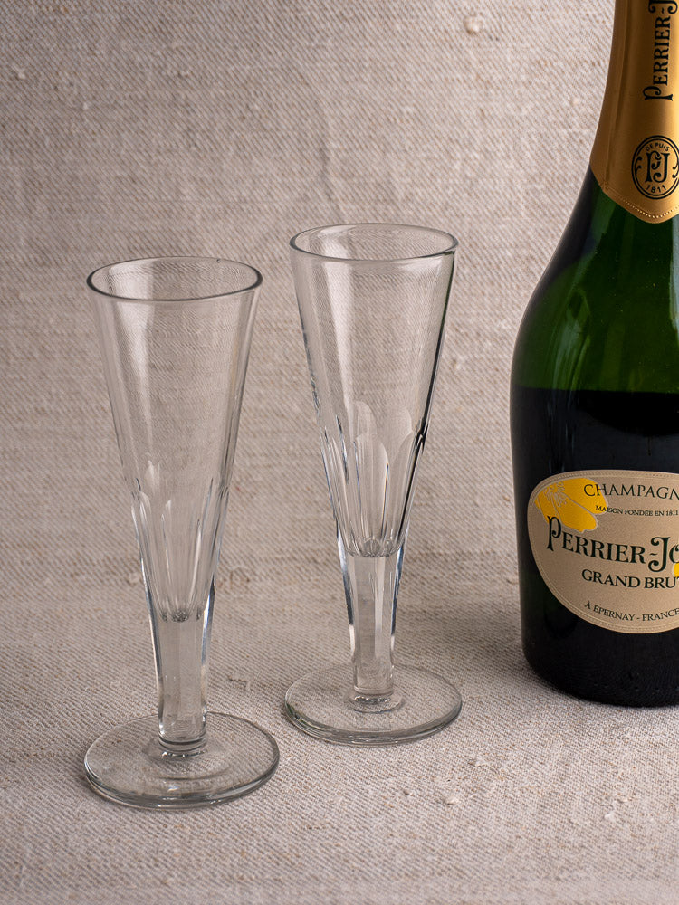 Six antique French cut crystal champagne flutes, early 19th century, on a textured surface with Perrier-Jouët Grand Brut.