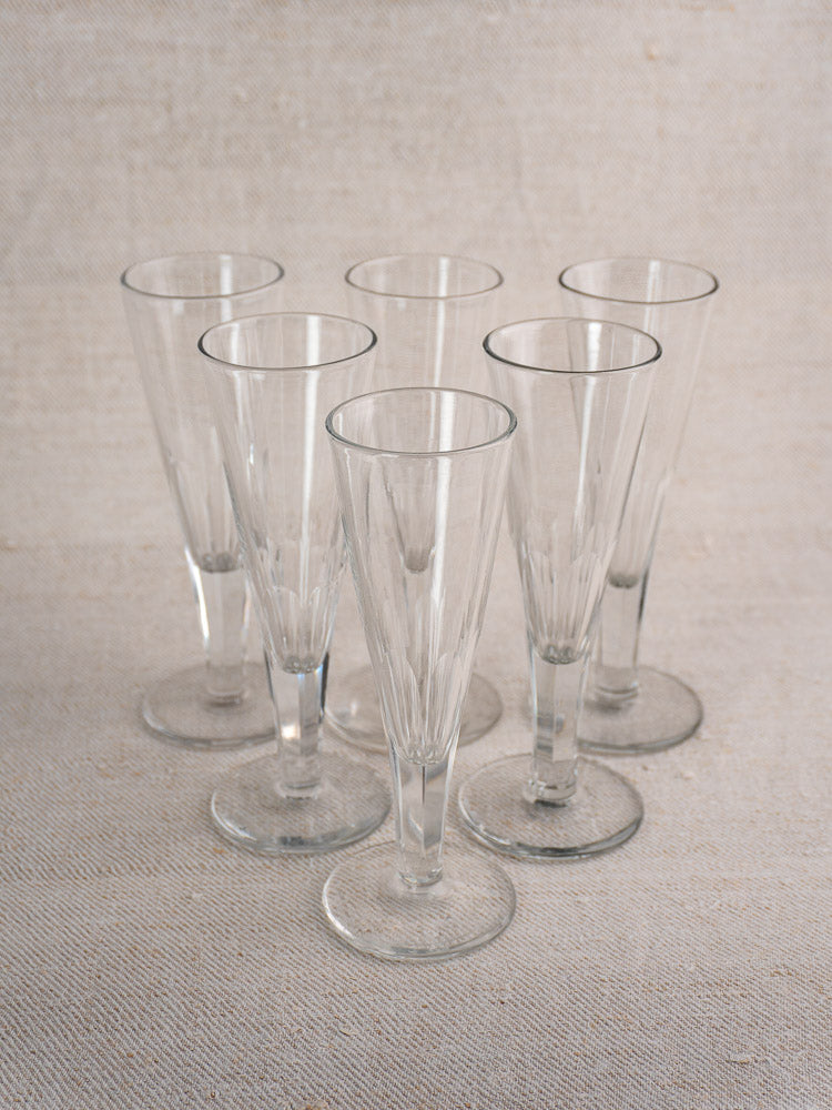 Set of six antique French cut crystal champagne flutes, early 19th century, grouped on neutral textured fabric.