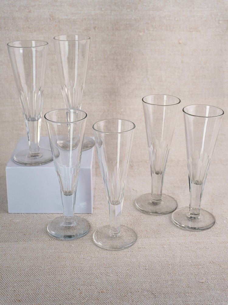 Set of six early 19th-century French cut crystal champagne flutes displayed on beige textured surface and white block.