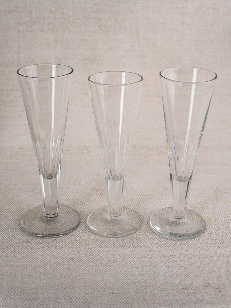 Set of six antique French cut crystal Champagne flutes in early 19th century style on beige textured fabric.
