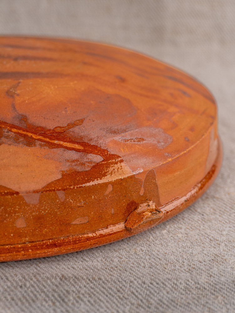 Antique French Tian with visible glaze drips, early to mid 20th century terracotta, on textured beige fabric.