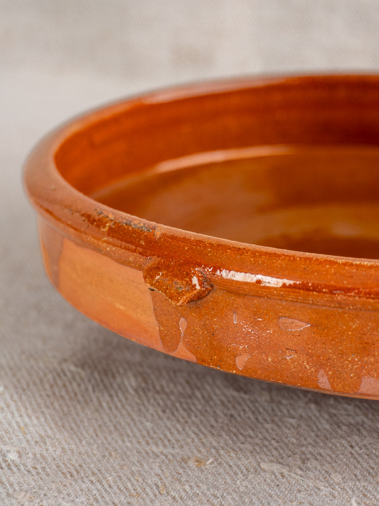 Antique French Tian, Provençal glazed terracotta baking dish with small rim chip on light textured fabric.