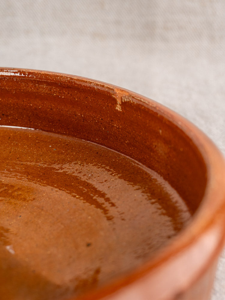 Antique French Tian, round glazed terracotta baking dish with drip mark on rim, on neutral fabric.