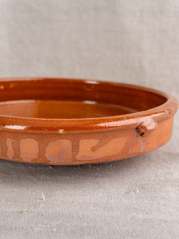 Antique French Provençal glazed terracotta tian with glossy brown finish and rustic rim on textured fabric background.