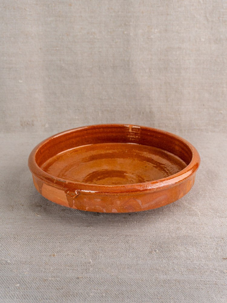 Antique French tian glazed terracotta baking dish on textured fabric, classic Provençal kitchen pottery style.