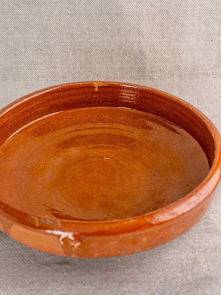 Antique French terracotta Tian baking dish with Provençal glaze on beige textured fabric backdrop.