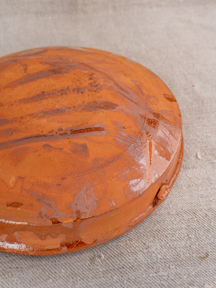 Antique French glazed terracotta Tian with brush marks and raised detail on textured beige fabric.