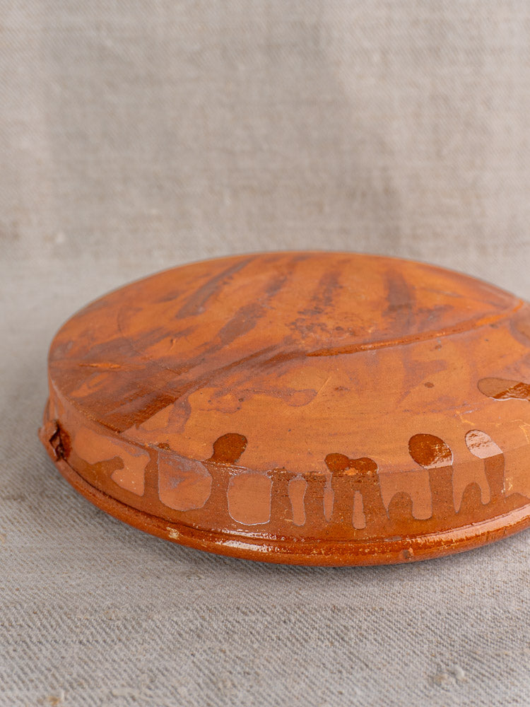 Antique French Tian, early to mid 20th century, glazed terracotta dish with painted motifs on beige textured fabric.