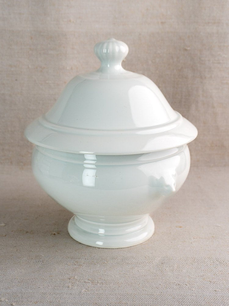 White French ceramic soup tureen with lid and lion head bowls on neutral fabric background.
