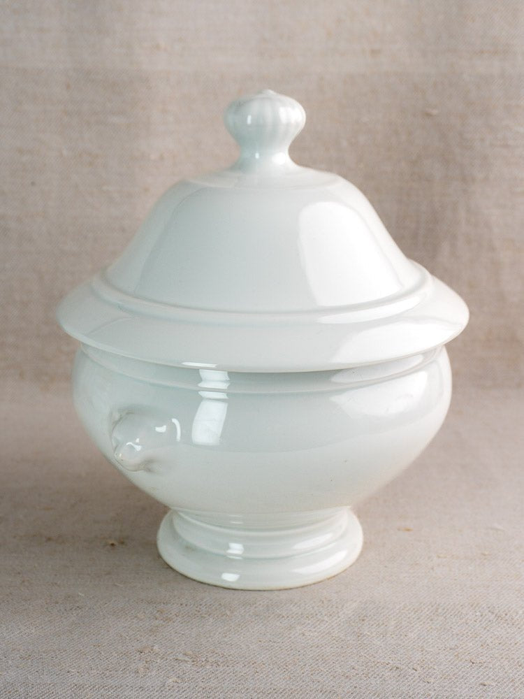 White ceramic French soup tureen with lid and handle on light beige fabric background.