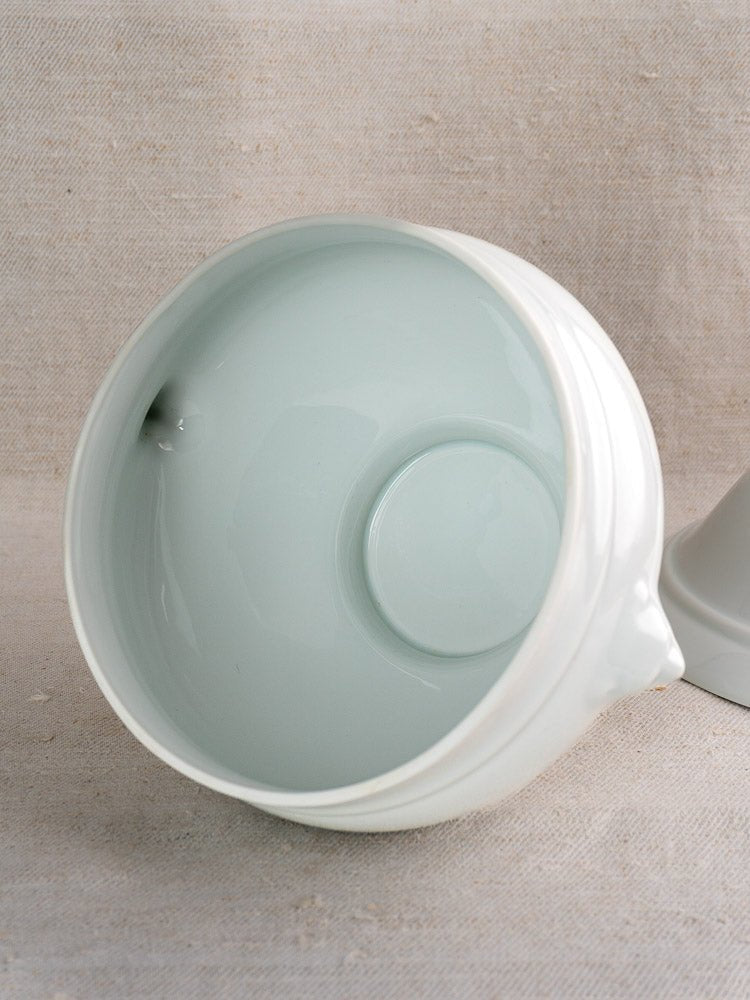Vintage French CNP lion head soup bowl with glossy white ceramic interior on beige fabric.