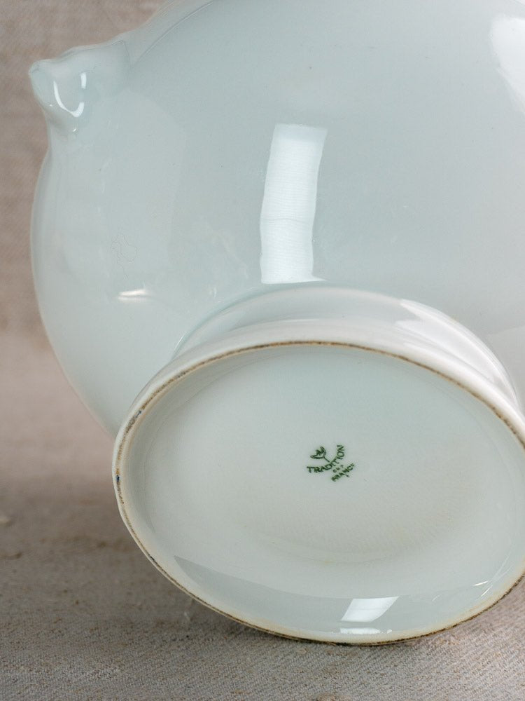 Underside of white porcelain tureen with green Chinese maker’s mark on light textured fabric.