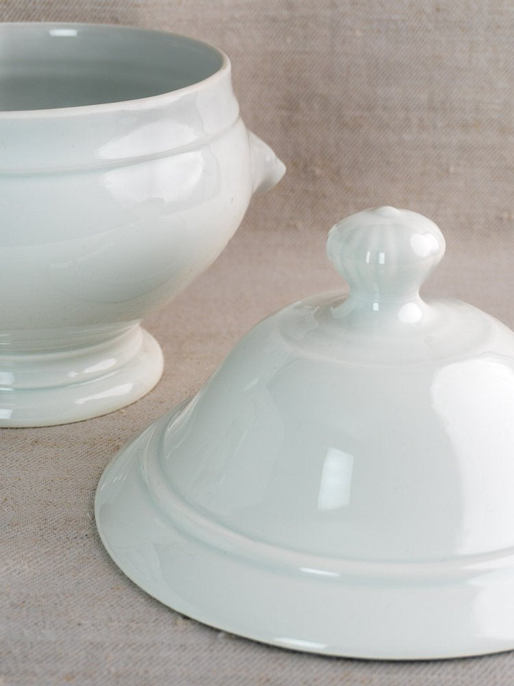 Vintage French white ceramic tureen with matching lid, displayed on beige textured fabric.